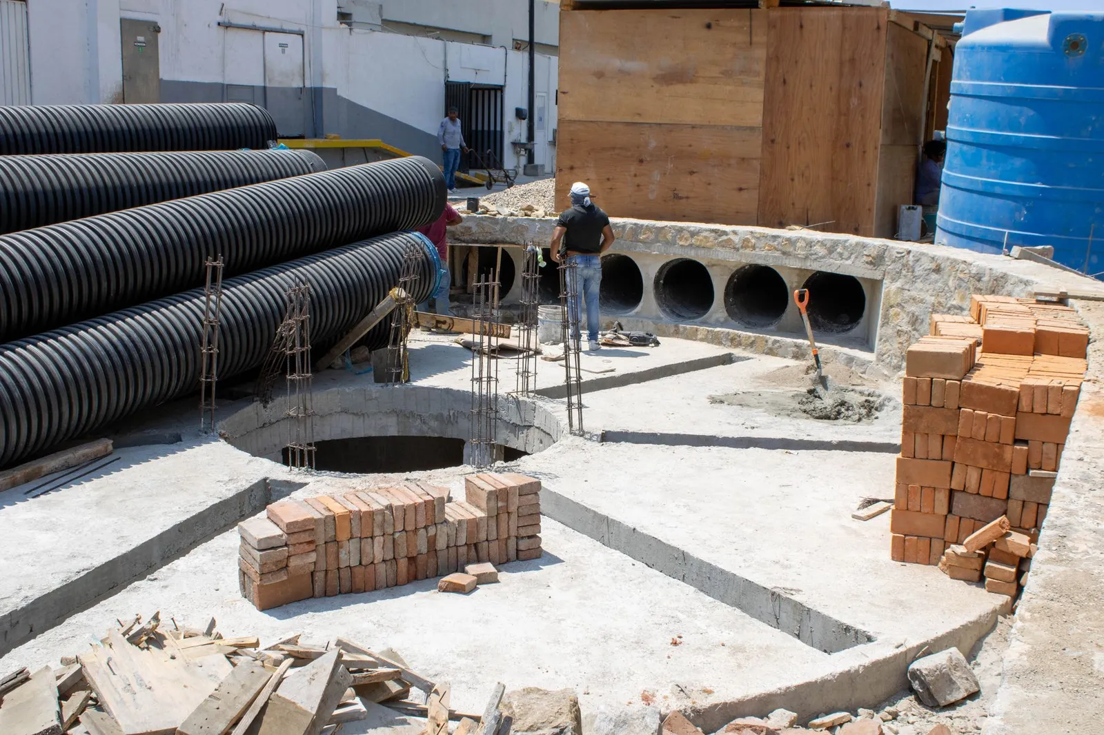 Workers at a construction site in Acapulco, Mexico, with stacked bricks and large pipes.